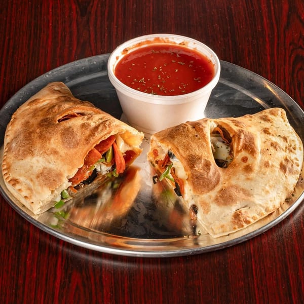 A calzone, cut in half to show its fillings, and a side of marinara sauce on a metal plate.