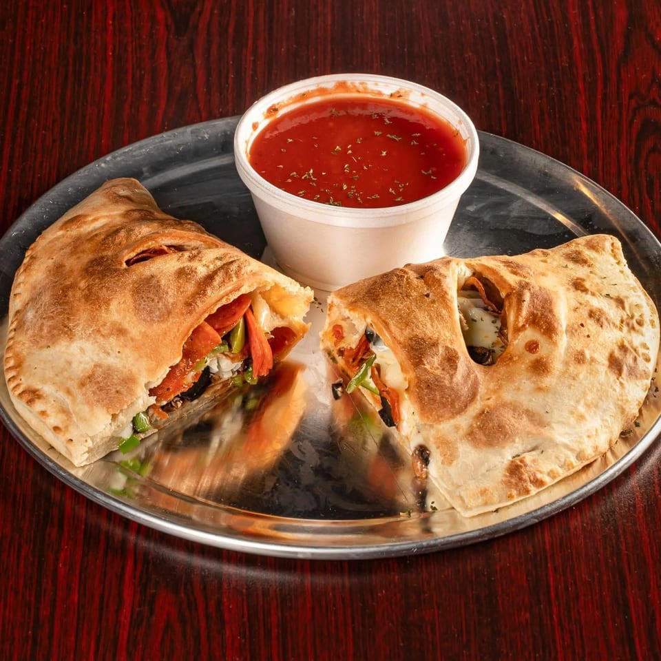 A calzone, cut in half to show its fillings, and a side of marinara sauce on a metal plate.