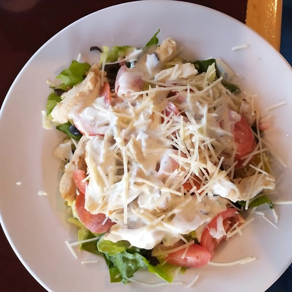 A chicken salad with lettuce, tomatoes, black olives, and shredded cheese, drizzled with dressing.