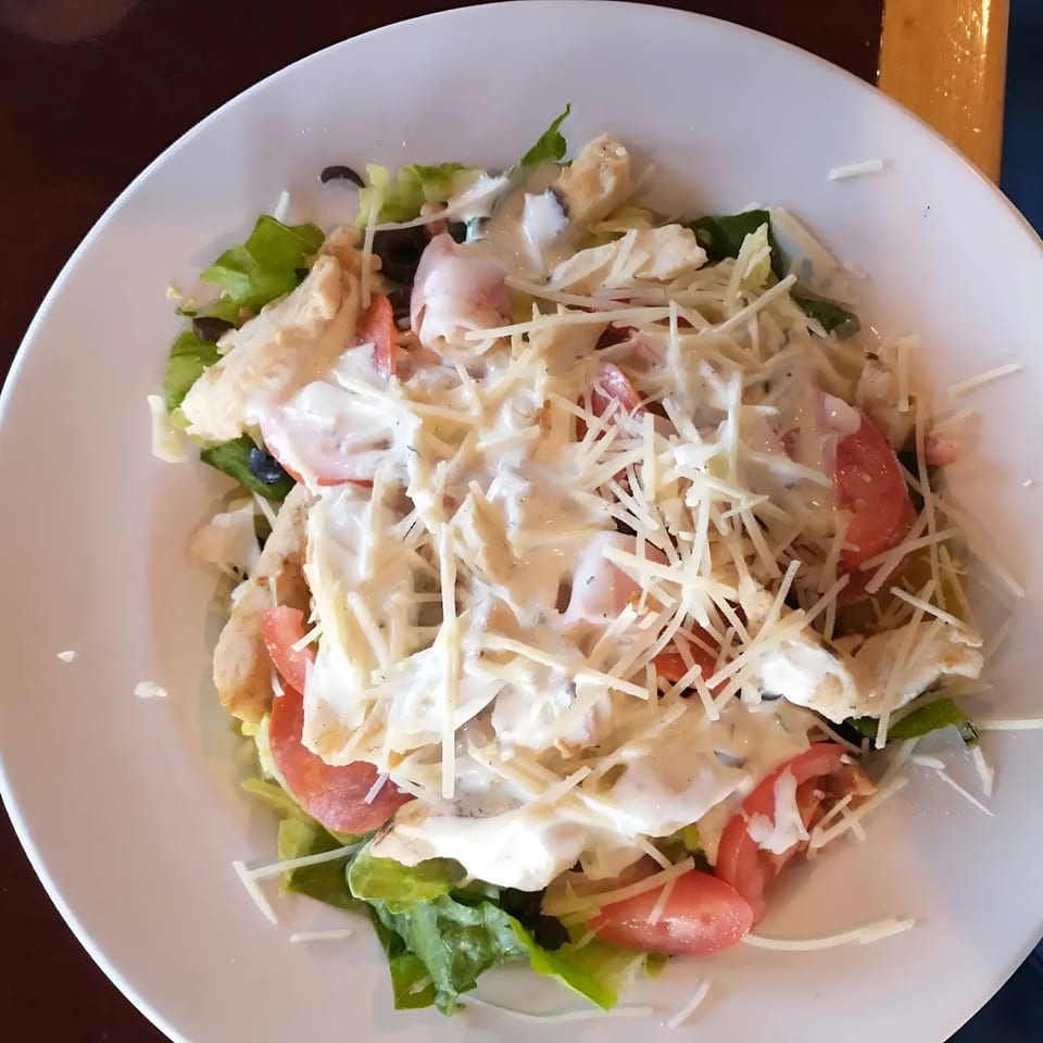 A chicken salad with lettuce, tomatoes, black olives, and shredded cheese, drizzled with dressing.
